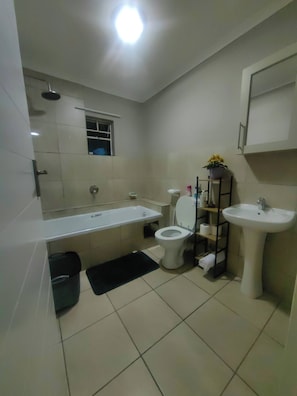 A modern bathroom with a bathtub, toilet, sink, and a small window. - Luxury Boutique Apartment in Secure Pretoria Estate (Pretoria)