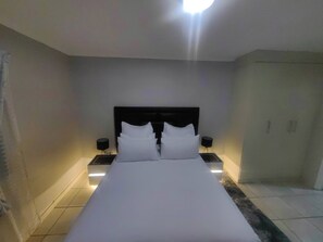 A hotel room with a large bed, two bedside tables, and a nightstand with a lamp.