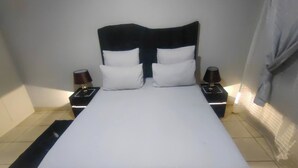 Quarto de hotel padrão com uma cama, duas mesas de cabeceira e um criado-mudo com luminárias.