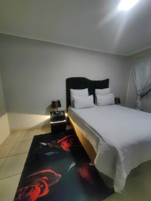 A bedroom with a bed, nightstand, lamp, and a wall-mounted light fixture. - Luxury Boutique Apartment in Secure Pretoria Estate (Pretoria)