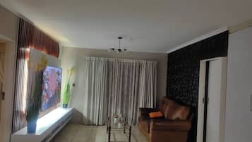 A living room with a sofa, a coffee table, a TV, and a window with curtains.