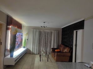 A living room with a sofa, a coffee table, a TV, and a window with curtains. - Luxury Boutique Apartment in Secure Pretoria Estate (Pretoria)