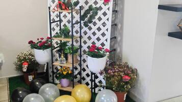 A room with a white lattice partition, potted plants, and balloons on a tiled floor.