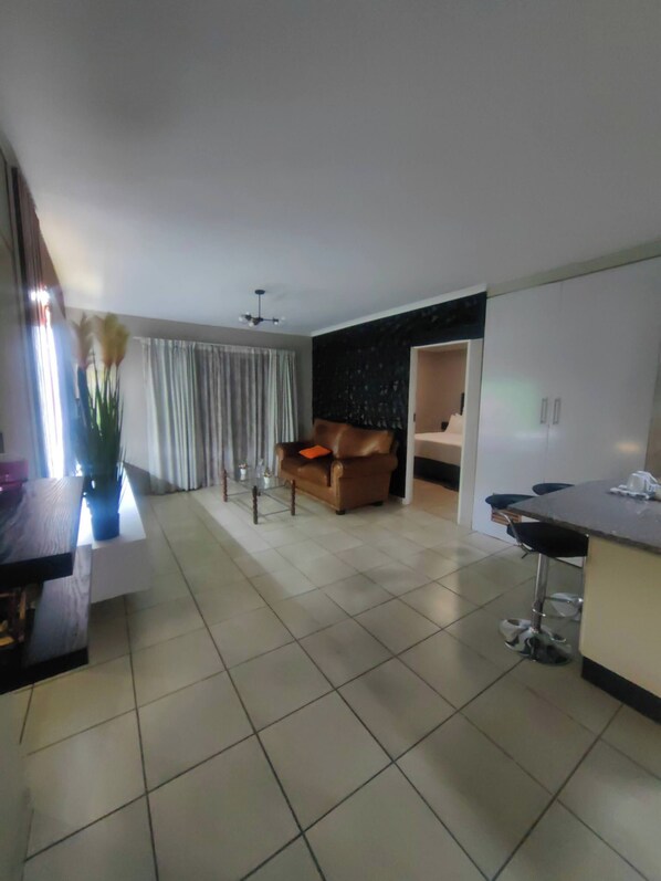 A modern living room with a sofa, a dining area with a table and chairs, and a kitchen area with cabinets.