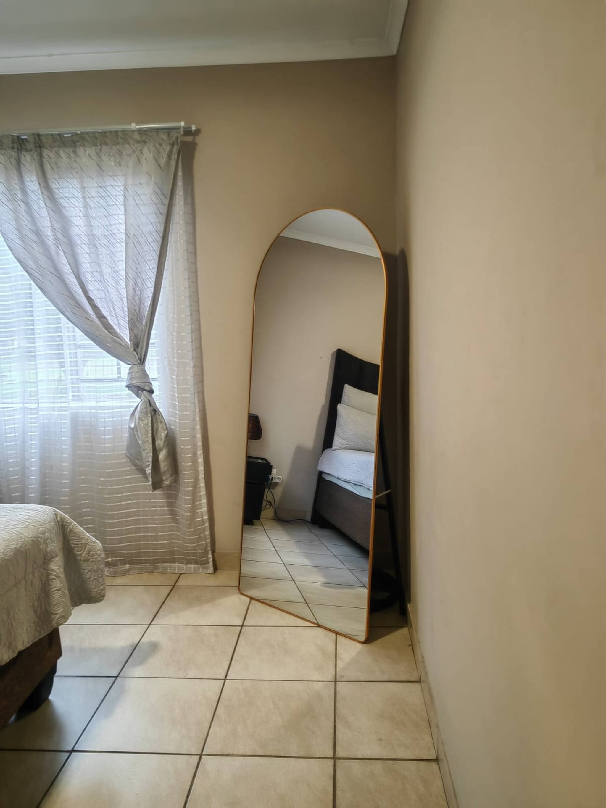 A bedroom with a bed, a mirror, and a window with curtains.