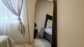 A bedroom with a bed, a mirror, and a window with curtains.
