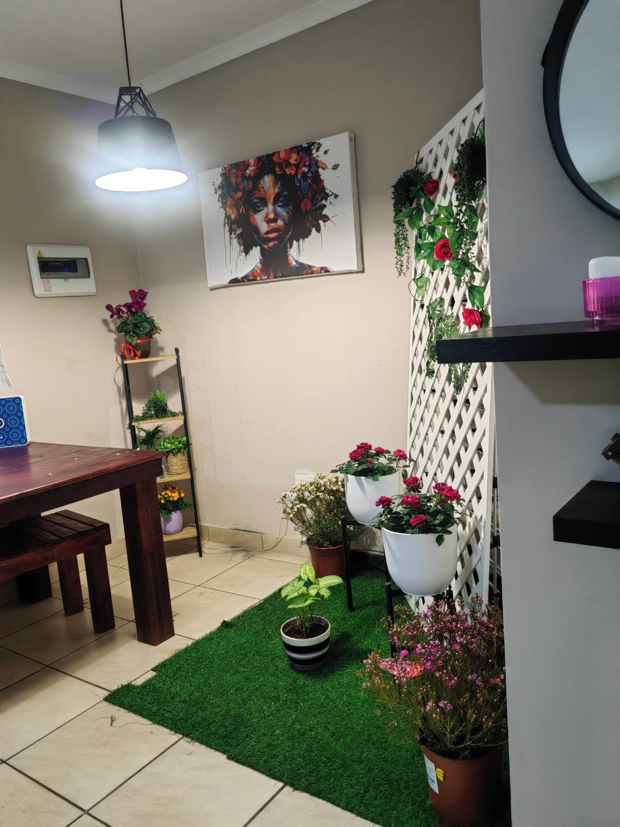 A dining area with a wooden table, chairs, a hanging light fixture, a wall-mounted thermostat, and a potted plant.