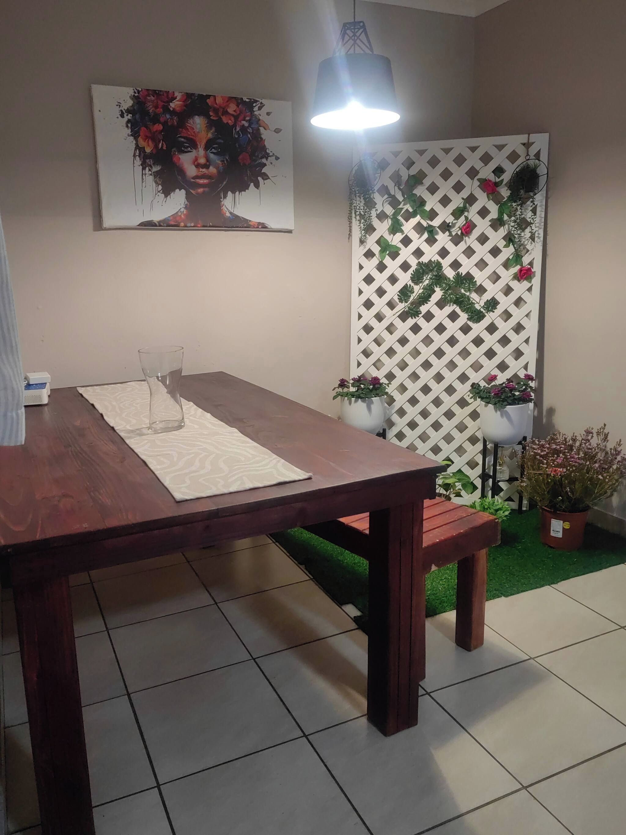 A dining area with a wooden table, a bench, a potted plant, and a wall-mounted light fixture.