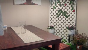 Uma área de refeições com mesa de madeira, um banco, uma planta em vaso e um aparelho de luz fixado na parede.