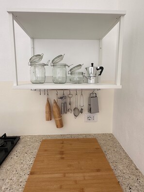 Cozinha com bancada, tábua de corte de madeira, um suporte com utensílios de cozinha e uma cafeteira.