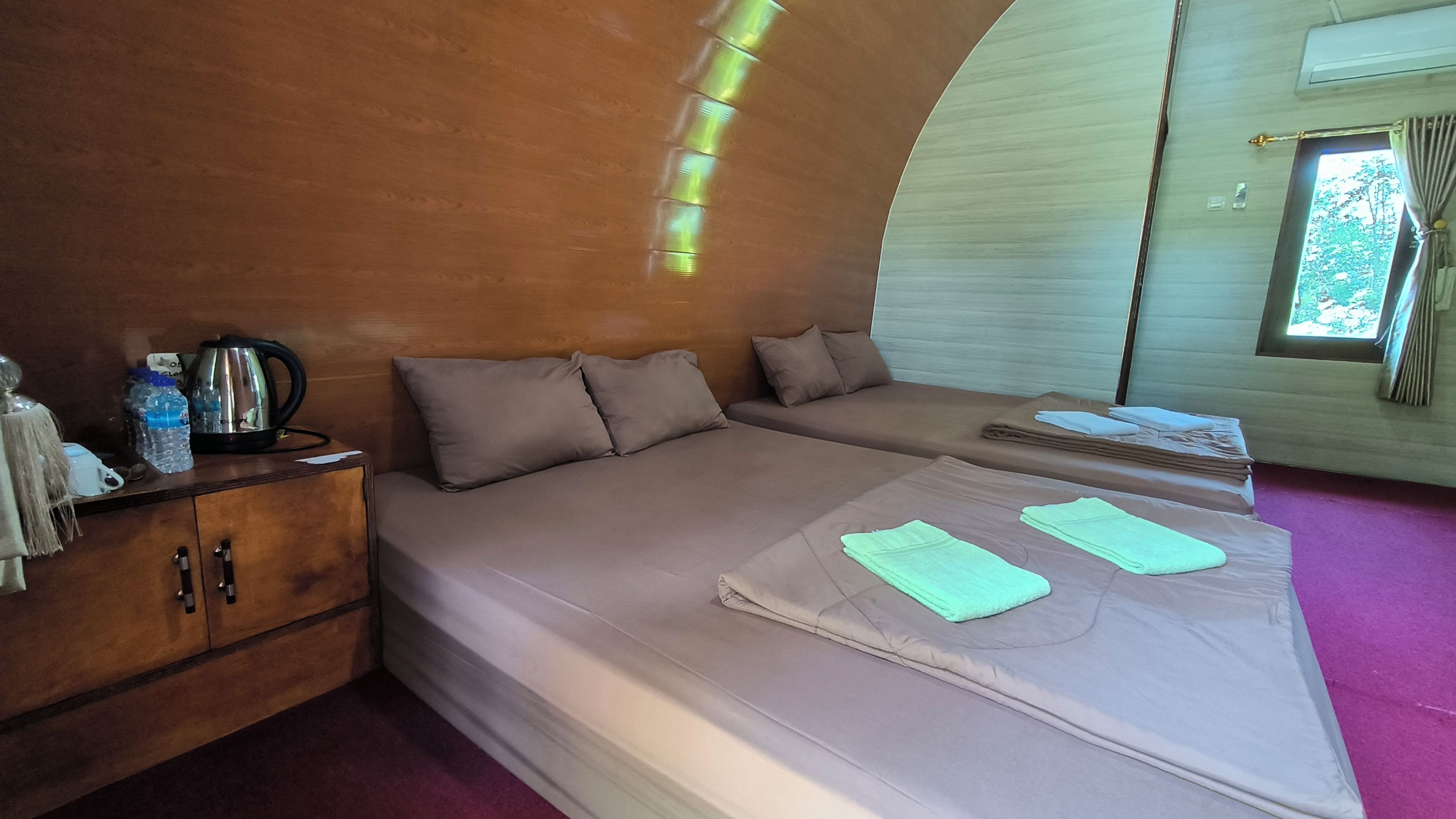 A room with a bed, a wooden cabinet, a kettle, and a window with curtains.