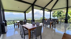 Un espacio al aire libre cubierto con mesas, sillas, barandilla y vistas a un paisaje montañoso.