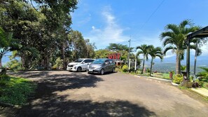 A road with two parked cars, a sign for a restaurant, and a view of the landscape. - Senja Kita Glamping (Salatiga)
