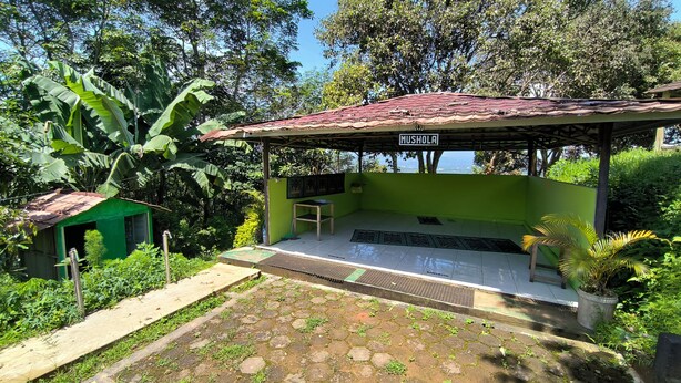 Un área de estar al aire libre cubierta con un letrero que dice 'MUSHOLA', rodeada de exuberante vegetación y vistas del paisaje.
