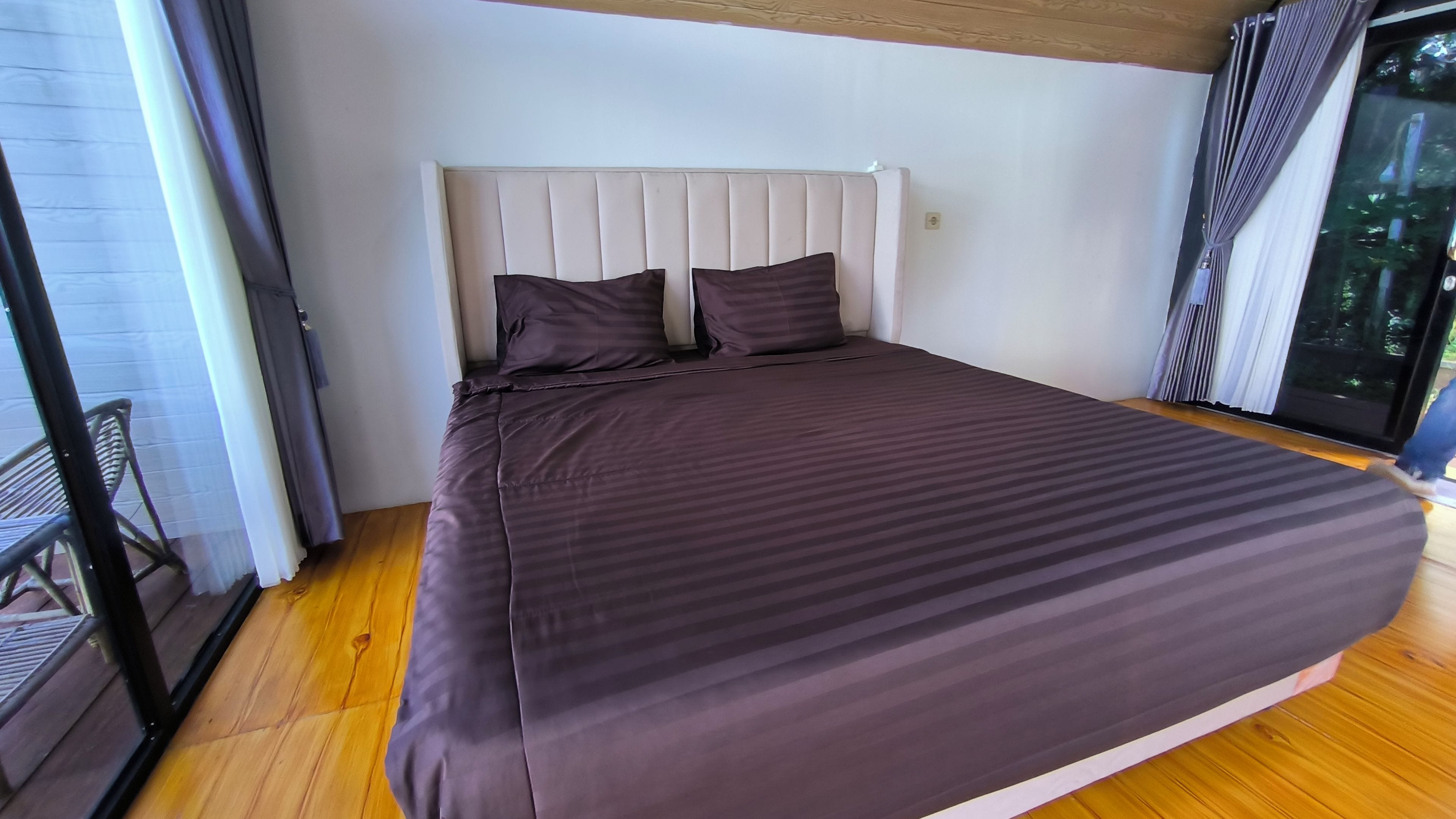 A bedroom with a bed, a headboard, and a view through a glass door.