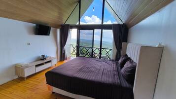 Un dormitorio con cama, televisión, una mesita con objetos y un balcón con vistas.