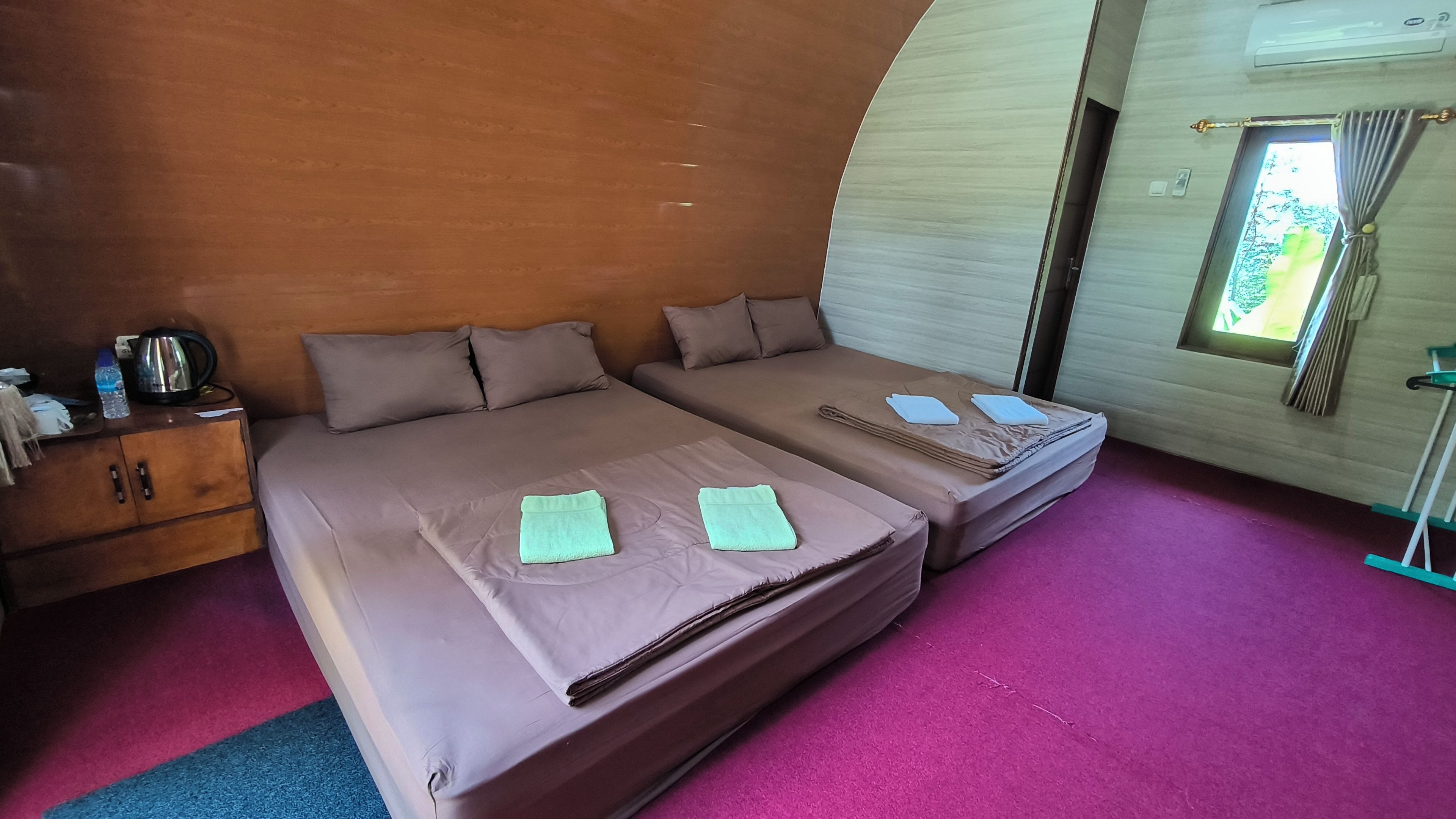 Una habitación con dos camas, un armario de madera, una tetera y una ventana con cortinas.