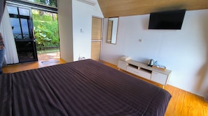 Un dormitorio con una cama grande, un televisor montado en la pared y un ventanal corredero que da a un espacio al aire libre.