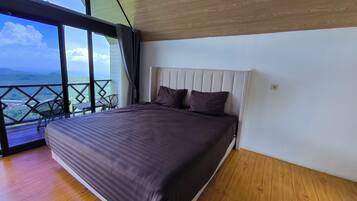 A bedroom with a large bed, a view of the outdoors, and a balcony with chairs.