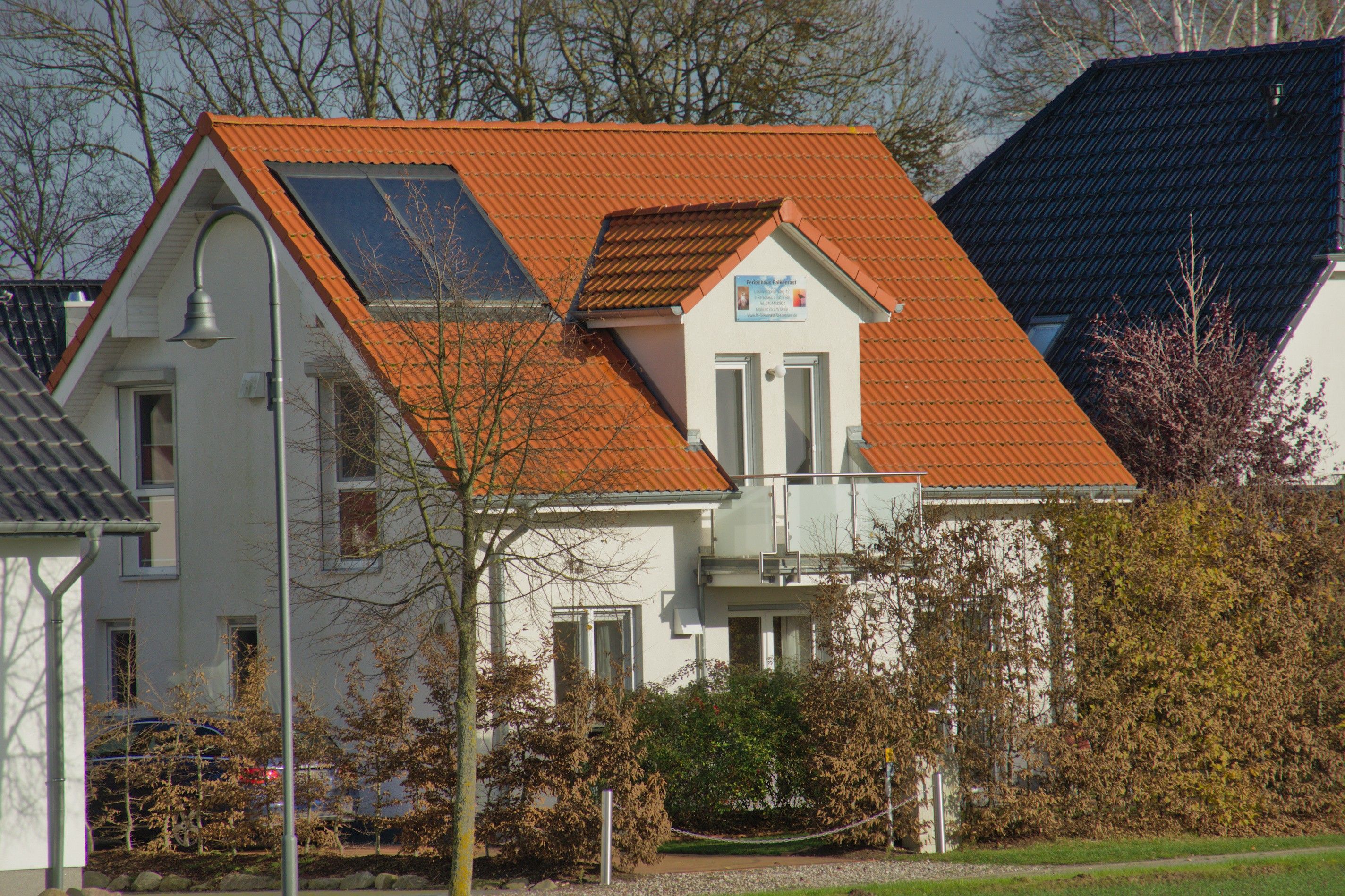 Ein zweistöckiges Haus mit rotem Ziegeldach, einem sichtbaren Balkon und einem kleinen Garten.