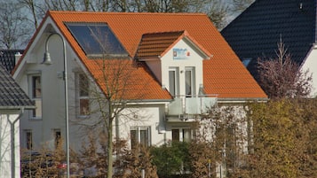 Ein zweistöckiges Haus mit rotem Ziegeldach, einem sichtbaren Balkon und einem kleinen Garten.