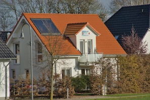 A two-story house with a red-tiled roof, a visible balcony, and a small garden area.