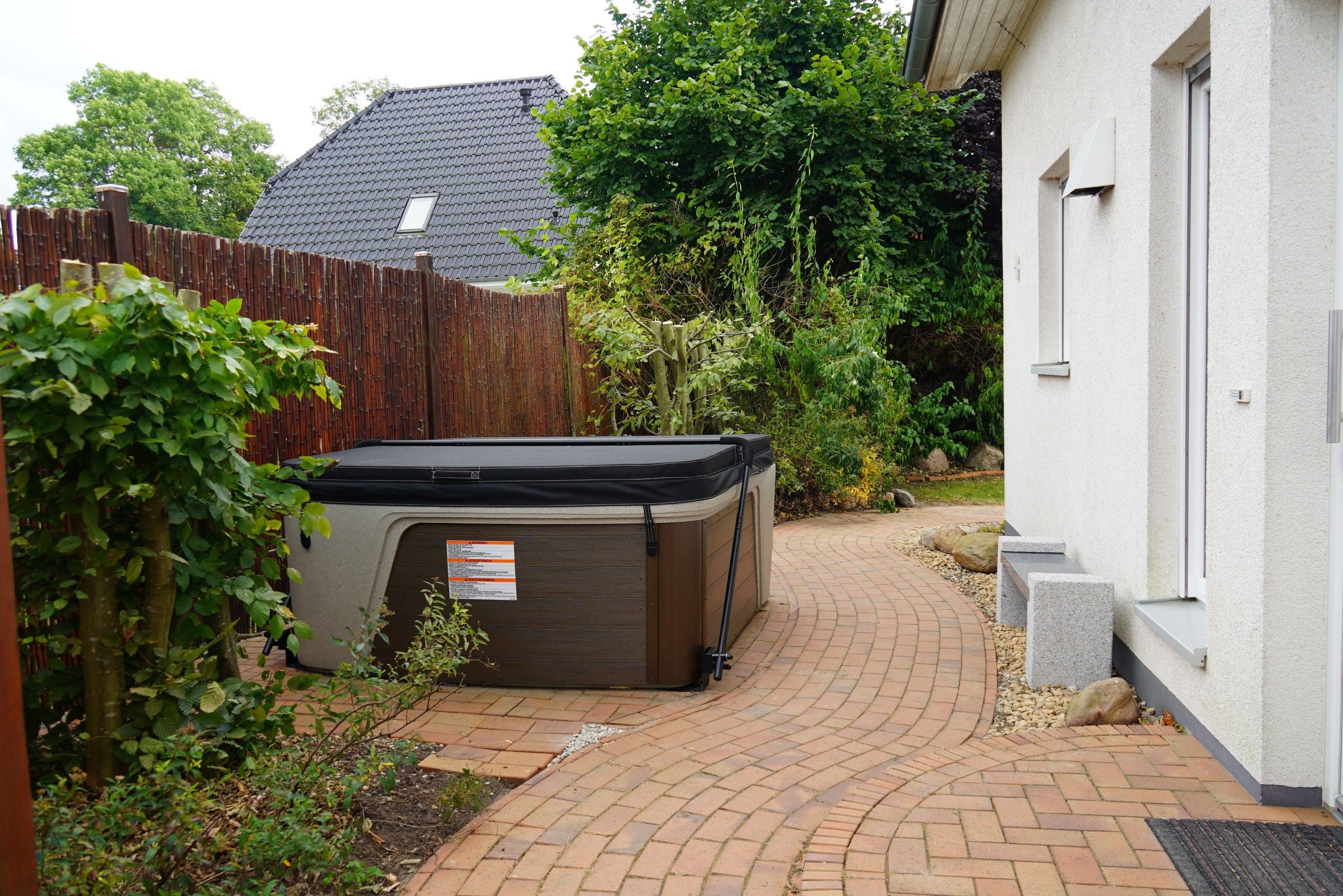 Ein Garten mit Whirlpool, Holzzaun und einem Ziegelweg, der zu einem Haus führt.