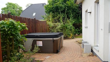 Ein Garten mit Whirlpool, Holzzaun und einem Ziegelweg, der zu einem Haus führt.