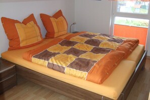 A bed with a quilt and pillows, a wooden nightstand, and a window with blinds.