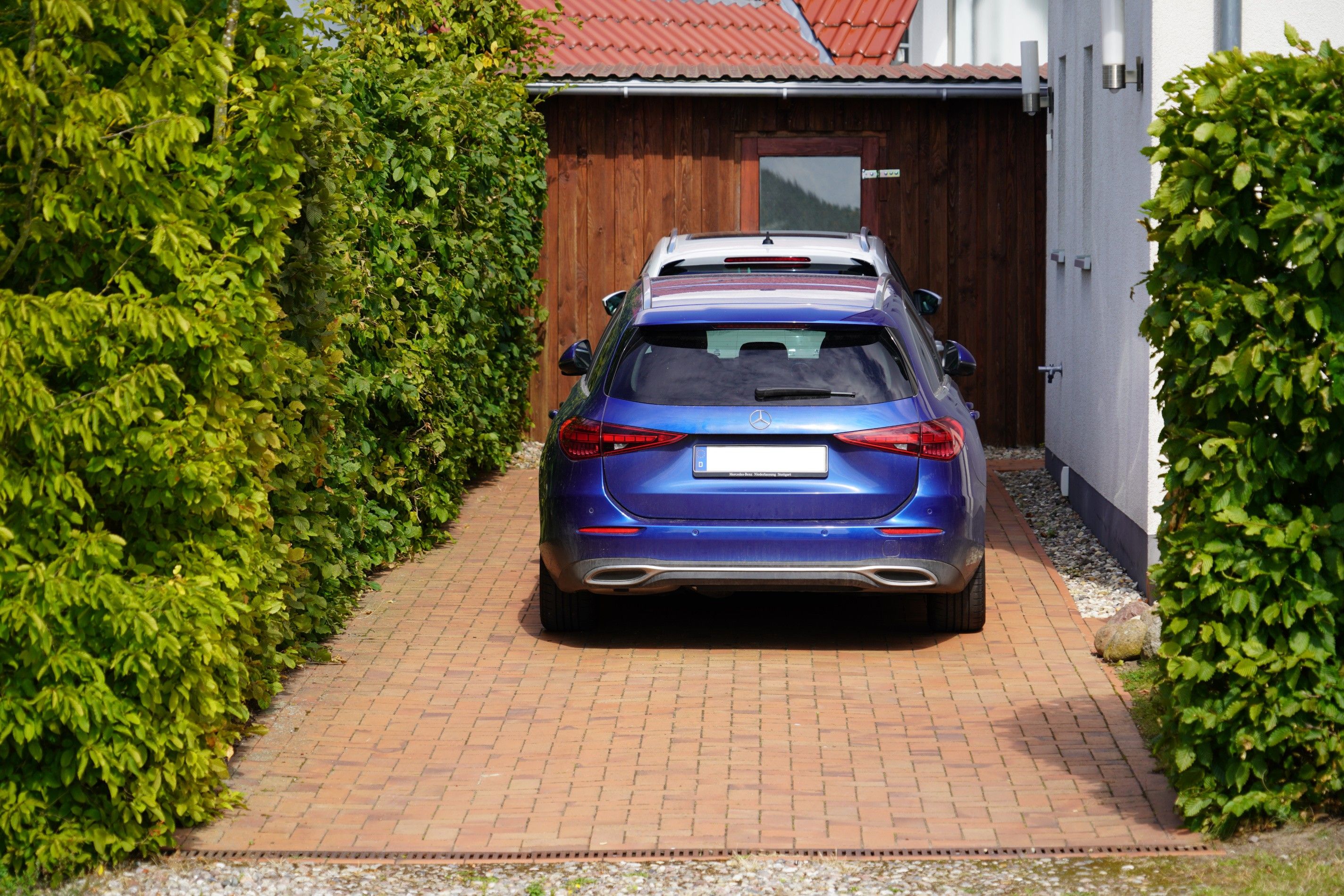 Ein blaues Auto auf einem gepflasterten Auffahrt, die zu einem Holztor führt.