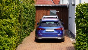 Um carro azul estacionado em um caminho de tijolos que leva a um portão de madeira.