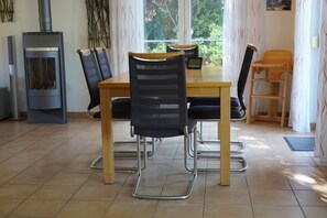 A dining area with a wooden table and chairs, a fireplace, and a view of greenery through the window.