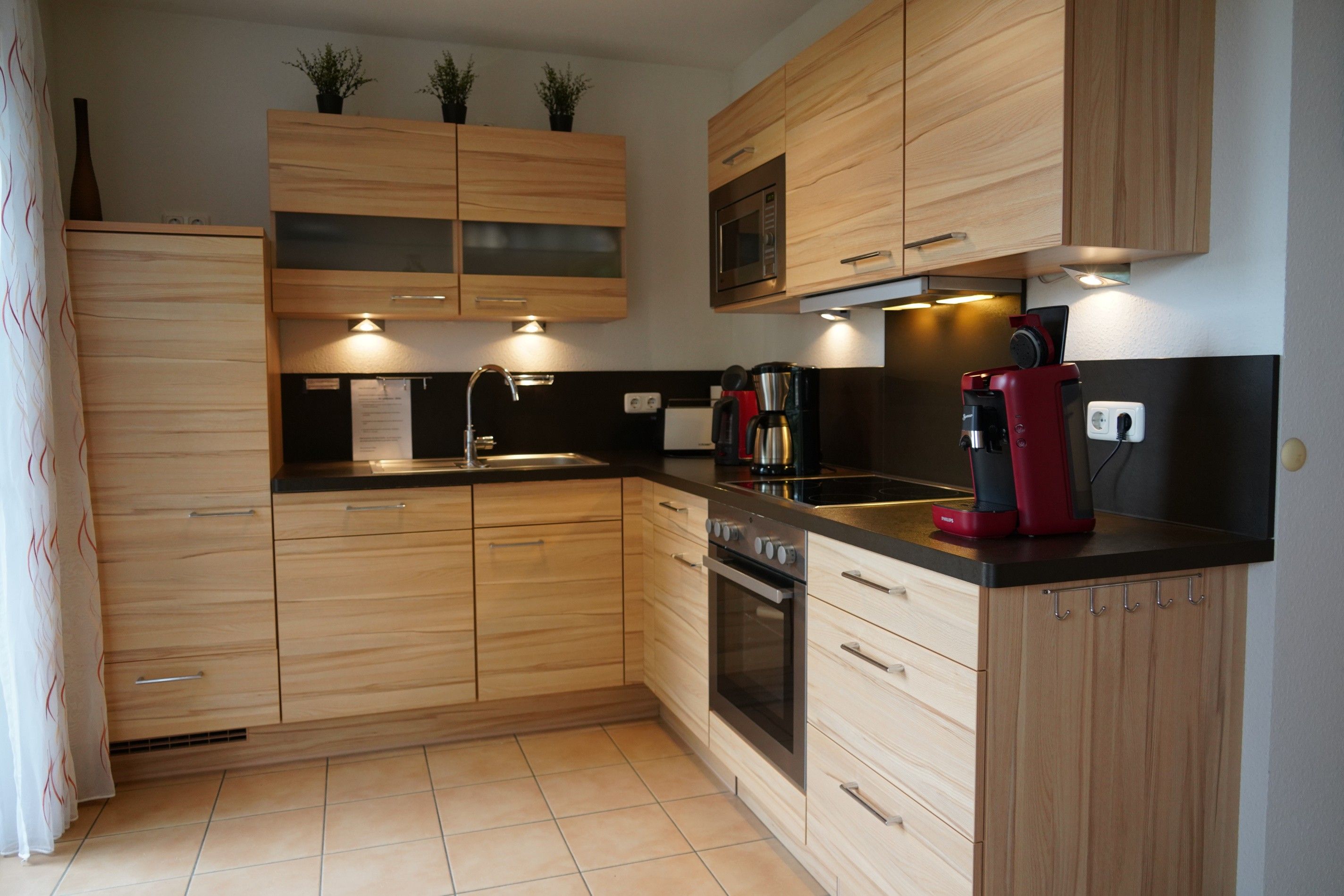 A modern kitchen with wooden cabinets, a built-in oven, a microwave, and a coffee maker.