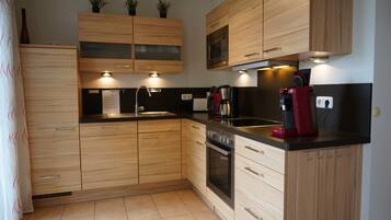 A modern kitchen with wooden cabinets, a built-in oven, a microwave, and a coffee maker.