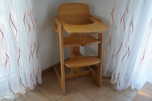 Ein hölzerner Hochstuhl mit Tablett vor einer Wand mit durchsichtigen Vorhängen.