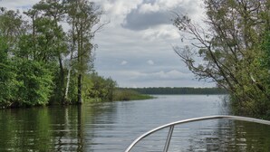 Água calma com árvores em ambas as margens, um barco em primeiro plano e céu nublado.