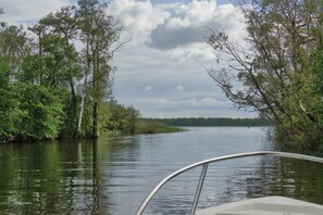 Ruhiges Gewässer mit Bäumen an beiden Ufern, ein Boot im Vordergrund und ein bewölkter Himmel.