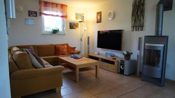 Ein Wohnzimmer mit einer Couch, einem Couchtisch, einem Flachbildfernseher, einem Kamin und einem Fenster mit Vorhängen.