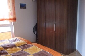 Ein Schlafzimmer mit einem Bett, einem Kleiderschrank, einem Wandventilator und einem Fenster mit Vorhängen.