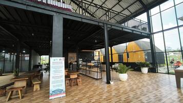 A spacious indoor area with a high ceiling, wooden flooring, and large windows offering views of the outside.