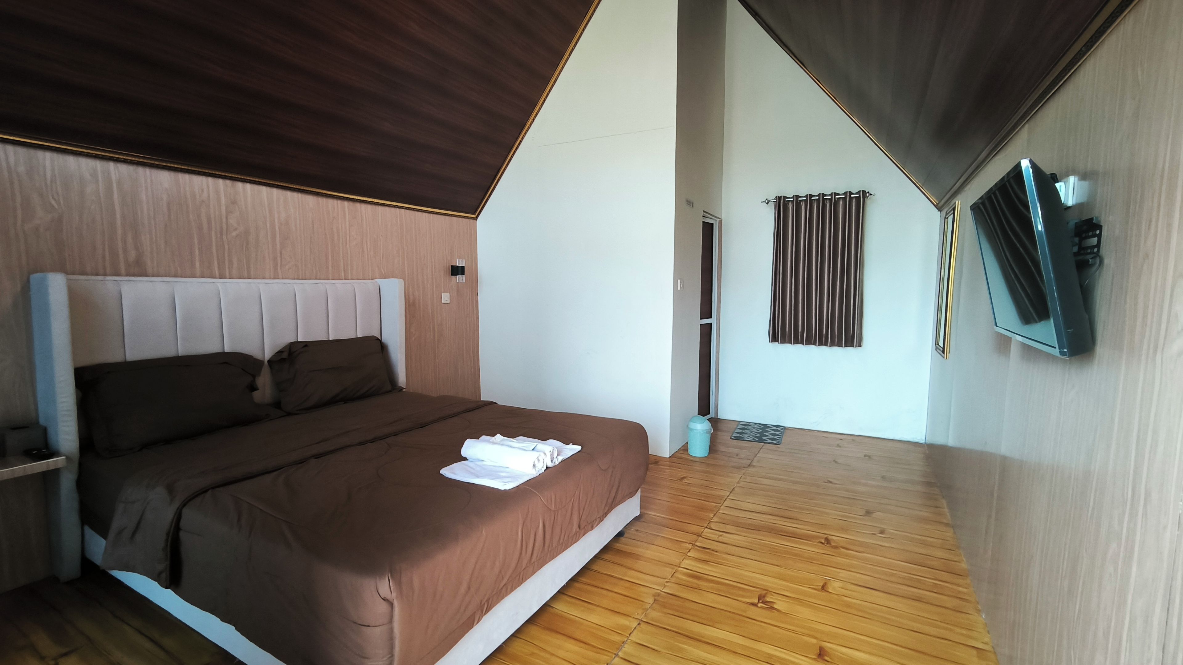 A modern bedroom with a bed, a flat-screen TV mounted on the wall, and a wooden floor.