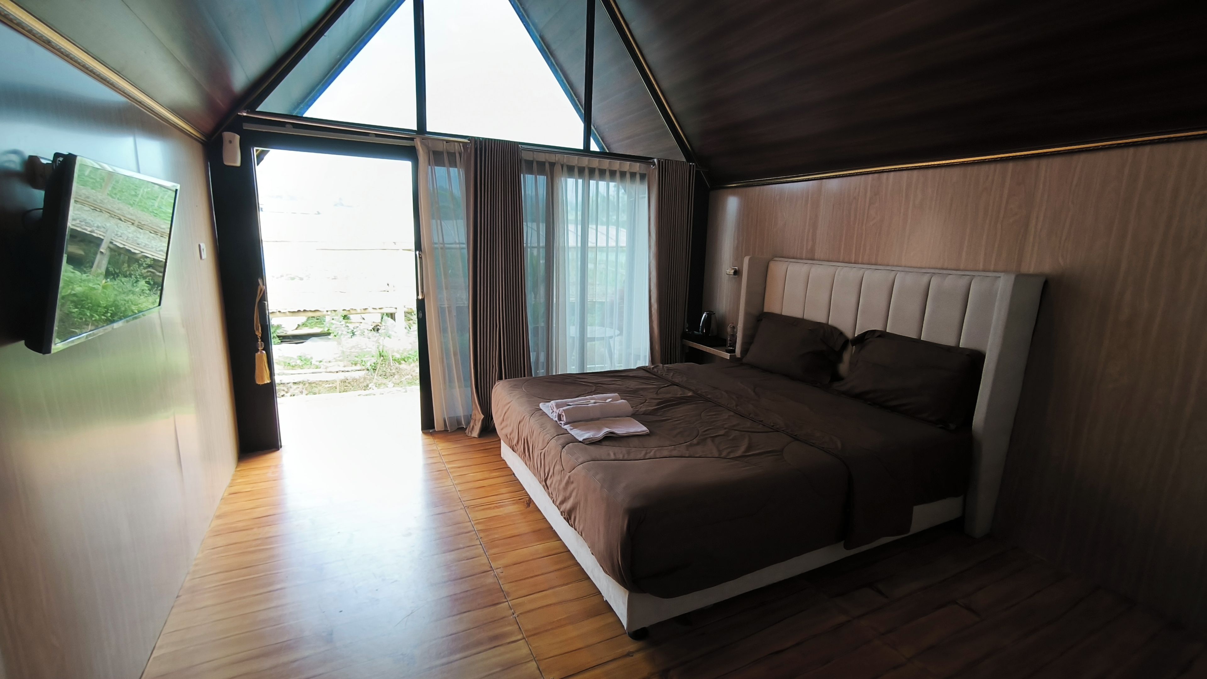 Ein modernes Schlafzimmer mit einem großen Bett, Holzboden, einem an der Wand montierten Fernseher und Blick ins Freie.