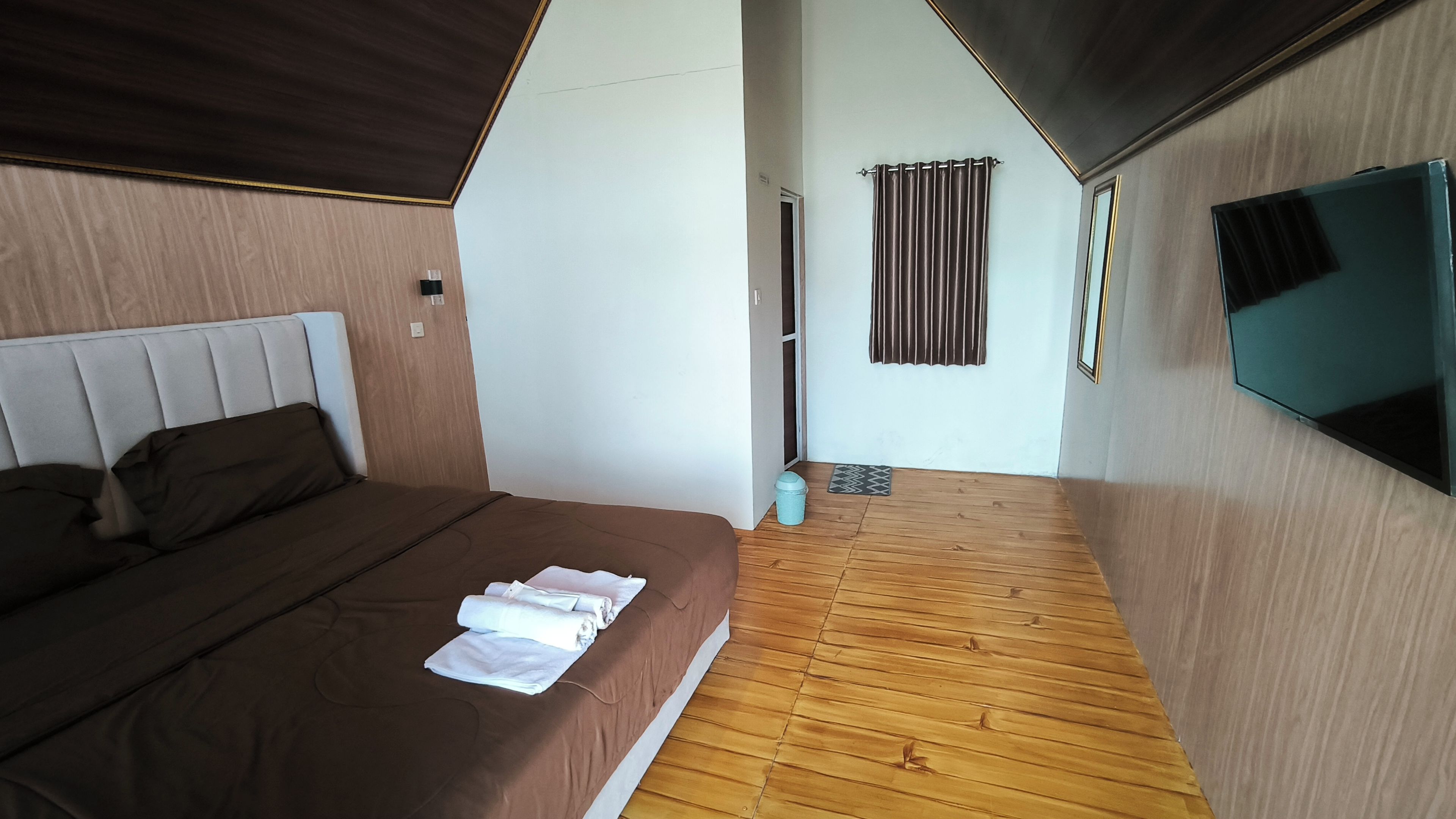 A hotel room with a bed, a television, a wooden floor, and a door leading to a balcony.