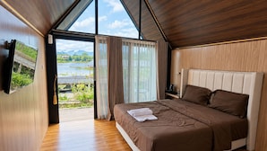 Quarto com uma cama grande, televisão e vista para um lago pela janela.
