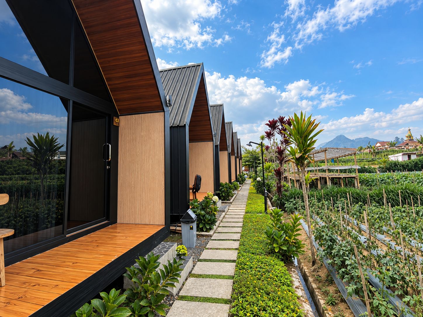 A modern building with a wooden deck and a pathway leading to a garden area with plants and a view of the mountains.