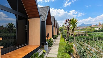 A modern building with a wooden deck and a pathway leading to a garden area with plants and a view of the mountains.