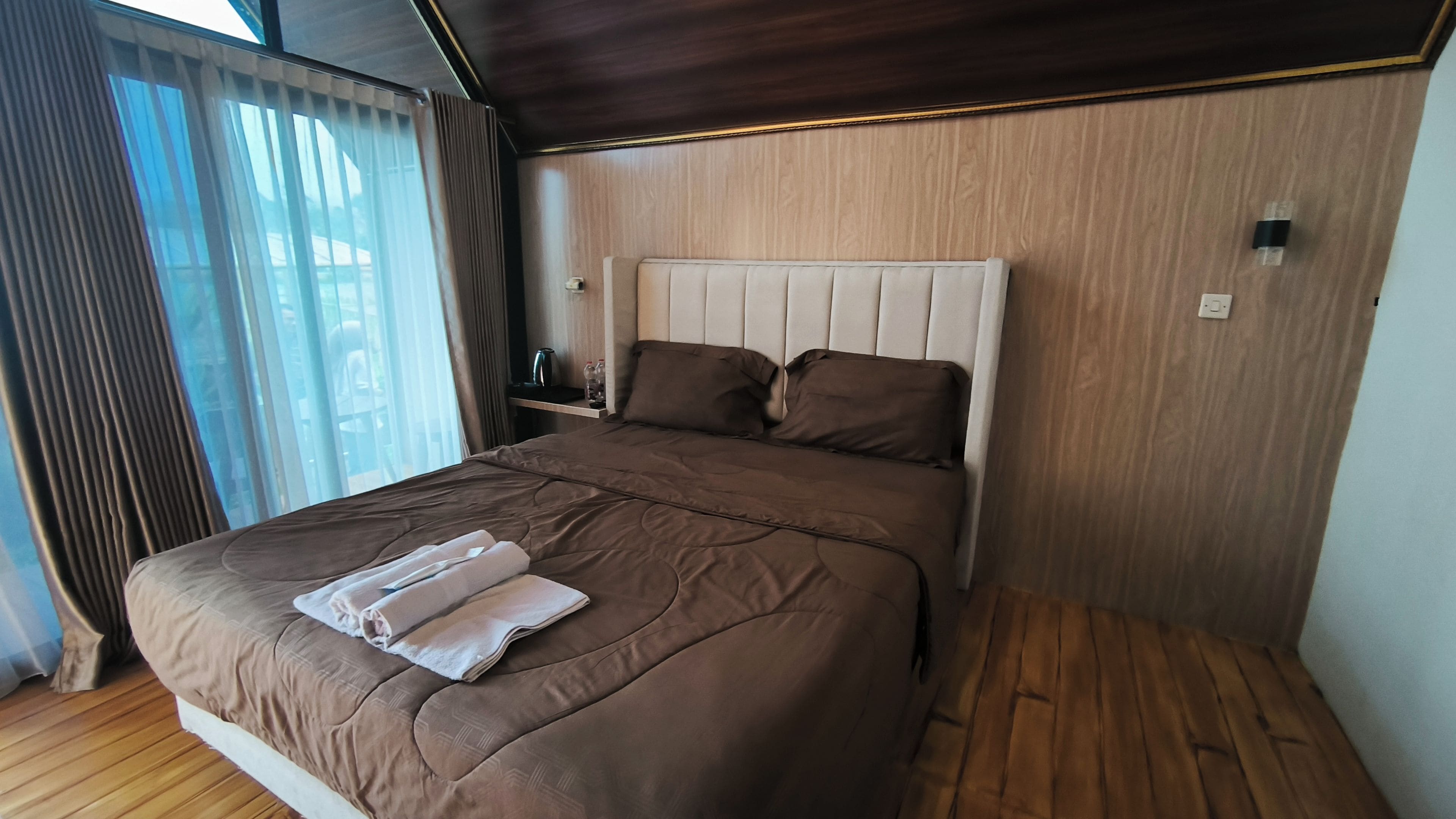 A bedroom with a large bed, a nightstand, and a window with curtains.