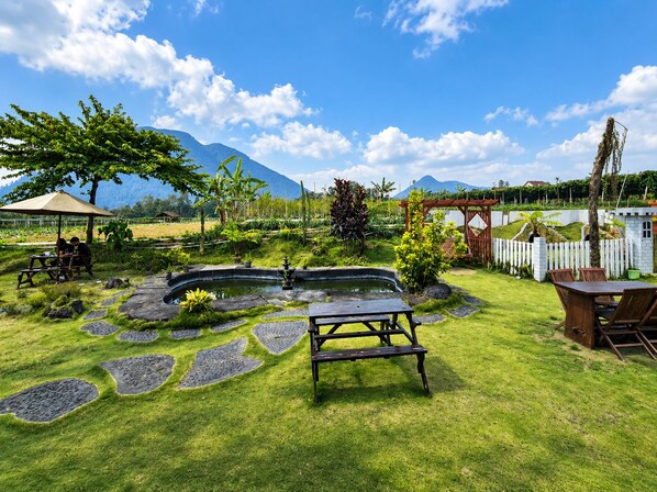 Un jardín con un estanque, mesas de picnic y una cerca blanca de piquetes.