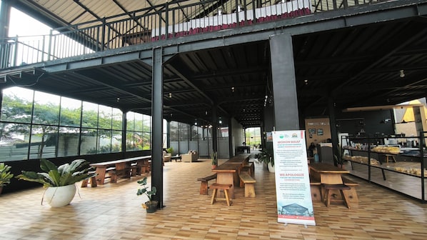 An indoor space with wooden benches and tables, large windows, and a signboard.