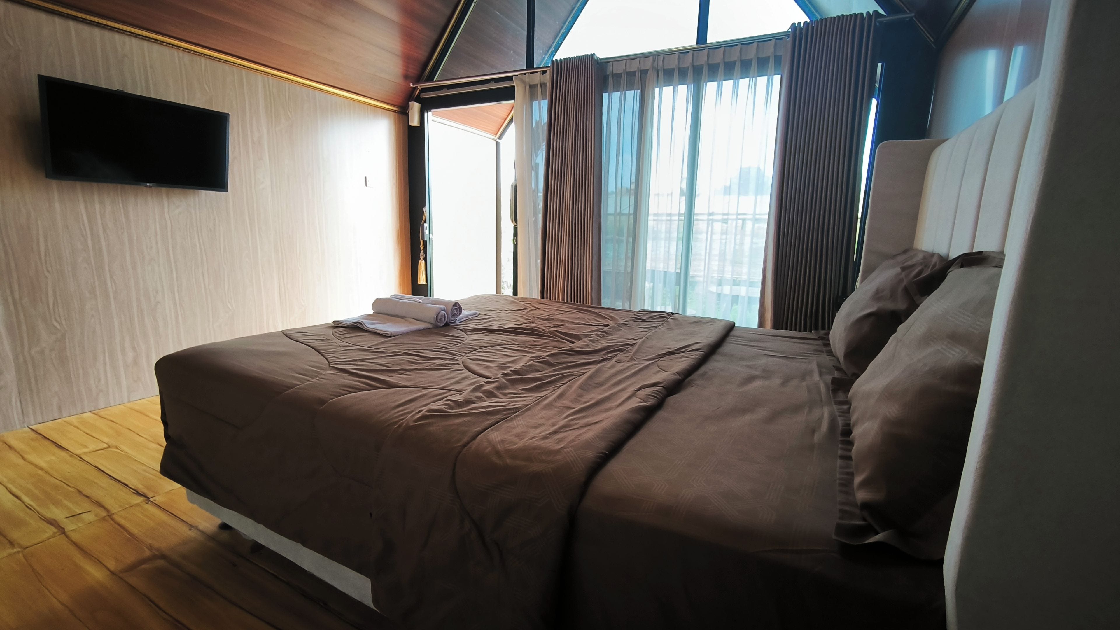 Una habitación de hotel con cama, televisión de pantalla plana y ventanas grandes con cortinas.